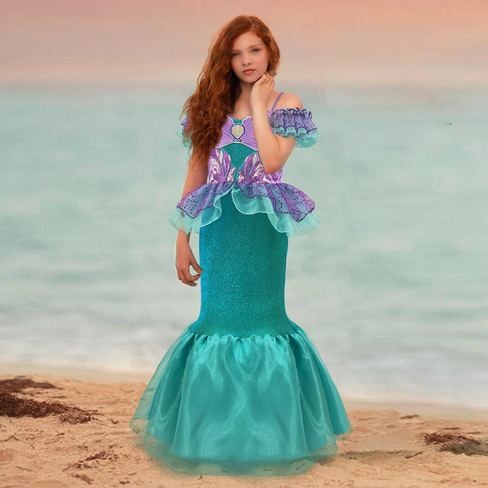Mermaid gown in teal and purple with ruffle sleeves and waist with shell applique on girl at a dreamy beach setting.