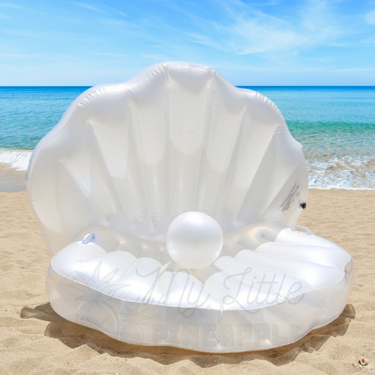 A white inflatable clamshell ride-on float sits on the sand at the beach on a sunny day.