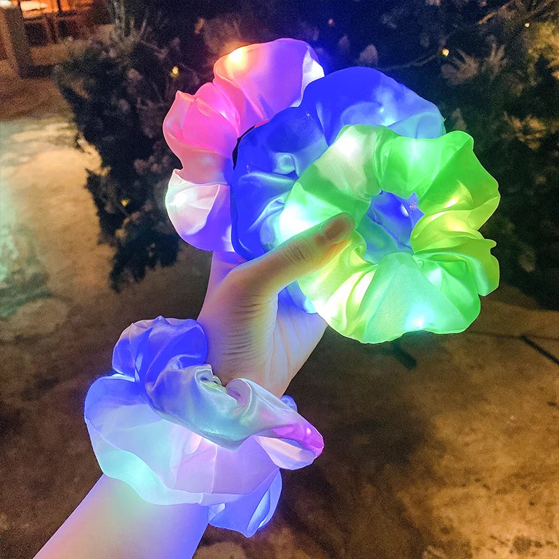 A hand holding three LED light-up hair scrunchies with two on the wrist..