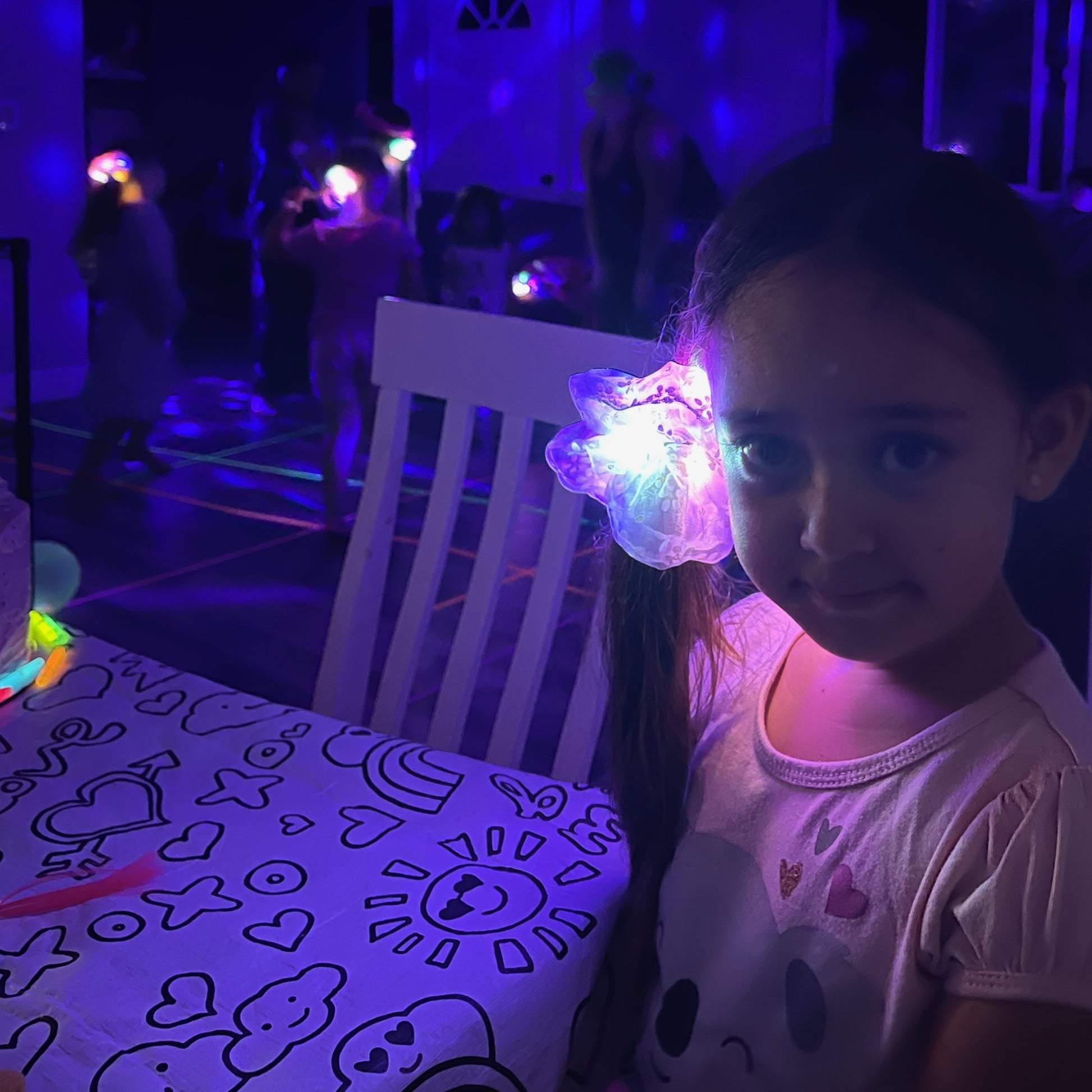 A little girl wear the LED light-up scrunchy in the dark with other scrunchies seen glowing in the background.